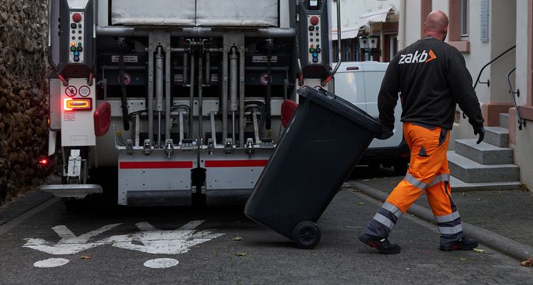in einer engen Gasse zieht ein Lader die leere Tonne vom Abfallsammelfahrzeug weg