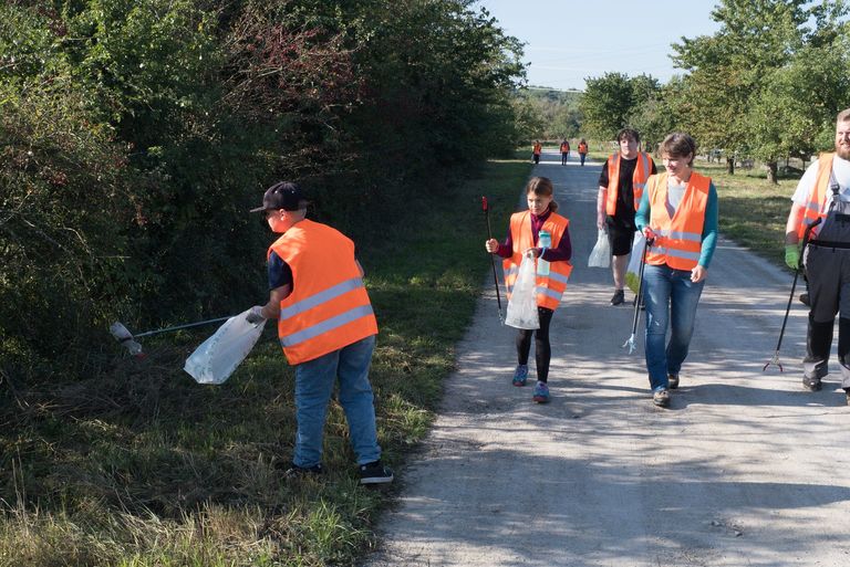  Kinder und Erwachsene in Warnwesten sammeln Müll am Straßenrand