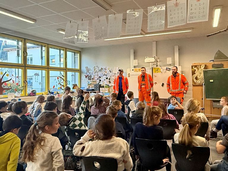 Drei orange gekleidete Müllwerker vor Schulklasse