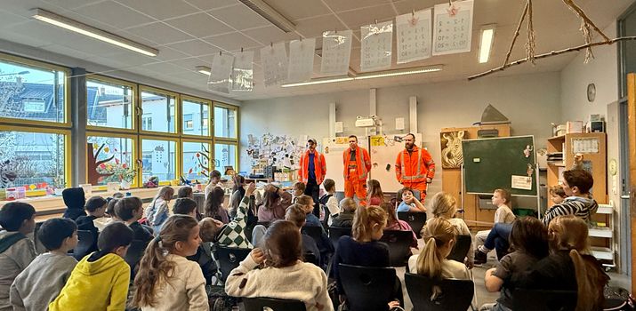 Drei orange gekleidete Müllwerker vor Schulklasse