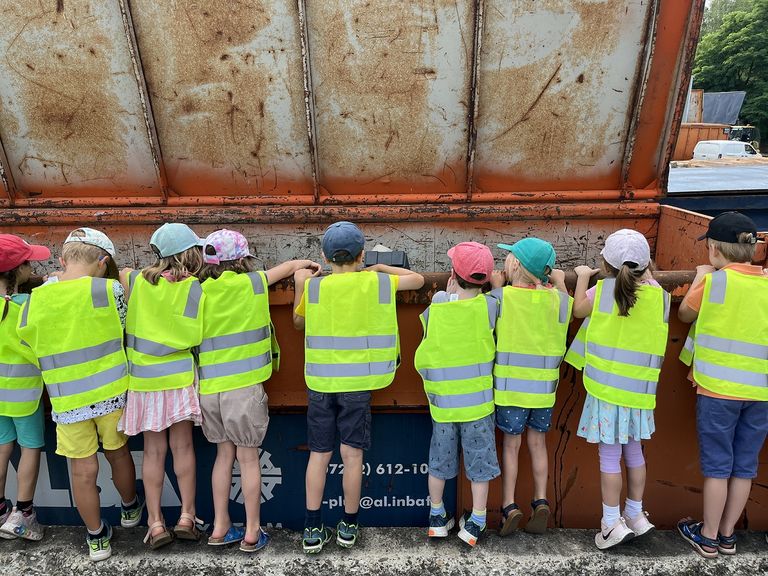 Bei einer Führung über den Wertstoffhof gibt es viel zu sehen. Kinder in gelben Warnwesten schauen in einen geöffneten rostigen Abfallcontainer