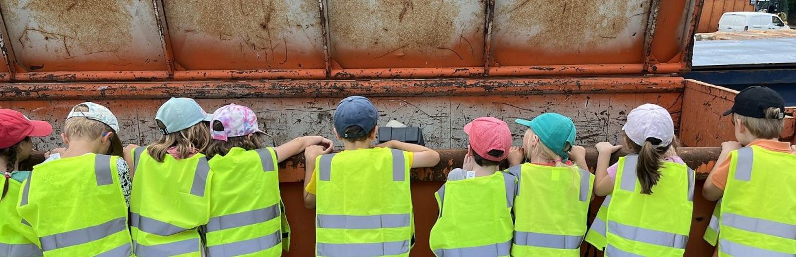 Kinder in gelben Warnwesten schauen in einen geöffneten rostigen Abfallcontainer