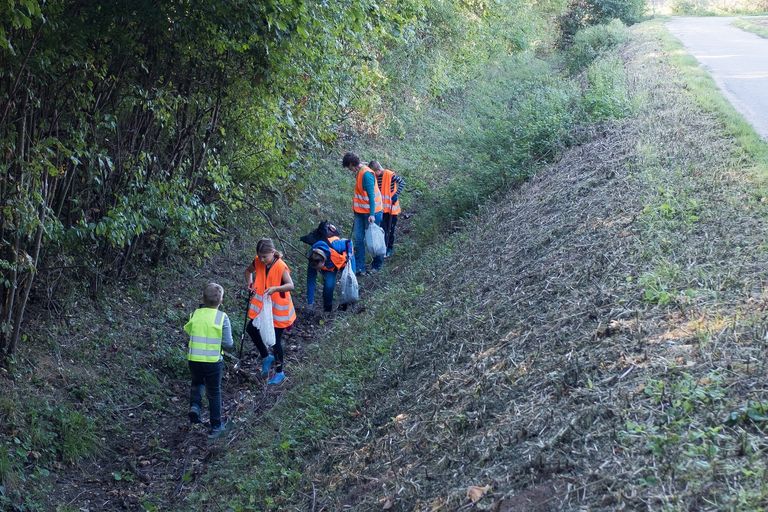 Kinder und Erwachsene in Warnwesten sammeln Müll im Straßengraben