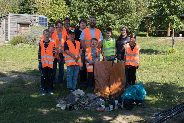 Kinder und Erwachsene in Warnwesten präsentieren eingesammelte Abfälle und prall gefüllte Mülltüten 