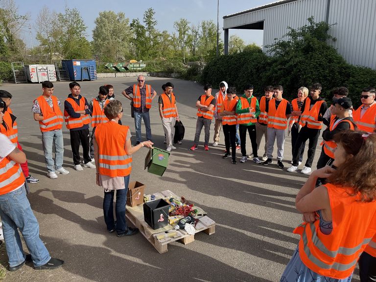 Menschengruppe in orangen Warnwesten auf einem Wertstoffhof